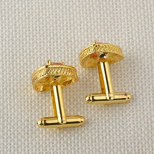 Detailed side view of gold-tone triangular cufflinks with orange enamel on fabric
