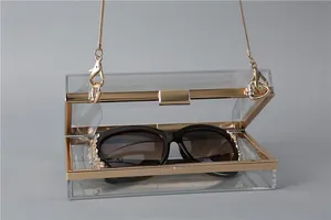Macro view of clear acrylic evening clutch bag with gold metal frame and chain strap