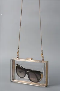 Macro shot of clear acrylic clutch bag with gold metal frame and interior sunglasses