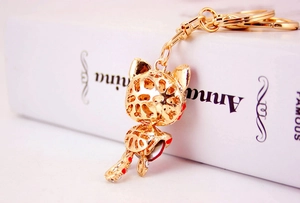 Close-up of golden hollowed-out cat keychain with red and white enamel details on a book