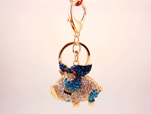 Detailed macro view of a gold-plated flying pig keychain with blue and white rhinestones