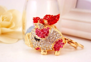 Detailed view of a gold flying pig keychain adorned with clear and red rhinestones