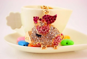 Detailed view of a flying pig keychain with pink rhinestones on a white tea saucer