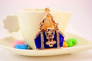 Blue enamel bag keychain with gold metal and rhinestones next to a small beige tea cup