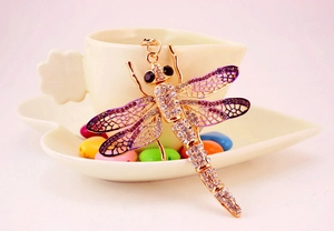 Macro shot of gold-tone dragonfly keychain with purple rhinestones on a heart dish