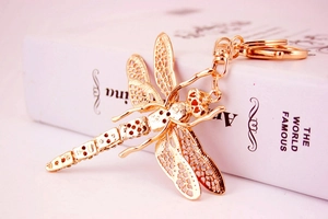 Macro view of a gold hollow dragonfly keychain with intricate cutout wings on a book