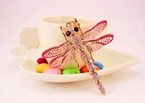 Macro shot of a golden dragonfly pendant with pink and clear crystals on a white ceramic saucer