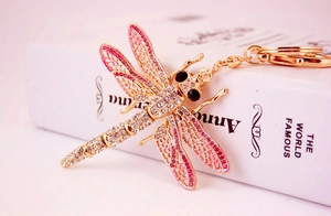 Detail of dragonfly keychain with pink crystals on gold metal over a book surface