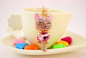Detail of pink lucky cat keychain with sparkling rhinestones and crystal on a ceramic cup