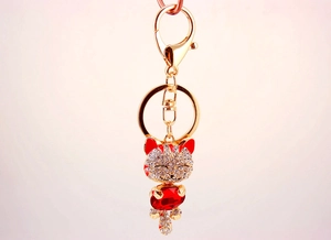 Close-up of golden lucky cat keychain with sparkling crystals and red pear-shaped stone