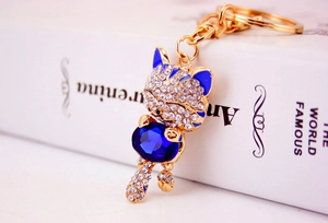 Macro detail of a gold-tone lucky cat keychain with blue stones and crystals