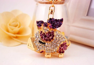 Macro detail of sparkling pig keychain with purple rhinestones on a golden ring