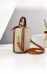Détail arrière d'un sac à main marron avec monogramme, clous et poignée en foulard de soie