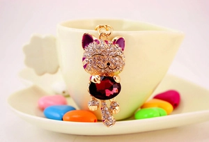 Macro detail of Maneki Neko keychain with red crystal and purple enamel accents