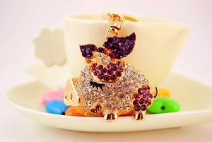 Close-up of a sparkling crystal flying pig keychain with purple rhinestones on gold base