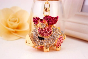 Close-up of flying pig keychain with pink and white rhinestones on golden metal