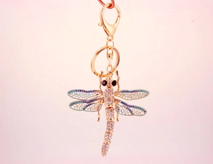 Detail of dragonfly keychain with blue rhinestones and gold lobster clasp on pink background