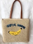 Detail of hand-woven straw tote bag featuring yellow banana embroidery and brown handles