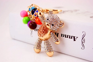 Detail of bear keychain with orange rhinestones and colorful beads on a golden metal base
