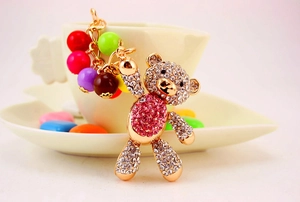 Detail of a golden bear keychain with rhinestones and colorful beads on a white surface