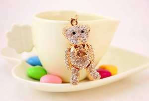 Close-up of luxury crystal bear keychain with gold bow hanging on a cream coffee cup