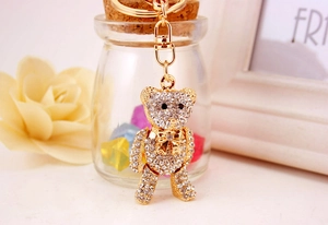 Close-up of golden teddy bear keychain with white rhinestones and decorative bow