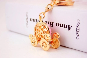 Close-up of golden pumpkin carriage keychain with pink enamel and crystals on white book