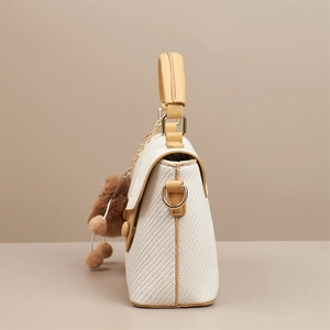Close-up of white woven handbag with yellow leather handle and brown pompom charm