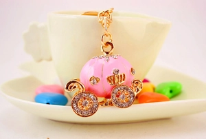 Close-up of pink enamel pumpkin carriage keychain with crystals on a white porcelain cup