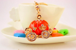 Detail of an orange pumpkin carriage keychain with gold alloy and shiny rhinestones
