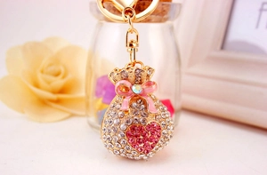 Close-up of a golden money bag keychain with white rhinestones and a pink enamel bow