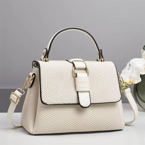 Close-up of cream textured handbag featuring gold metal hardware and detachable strap