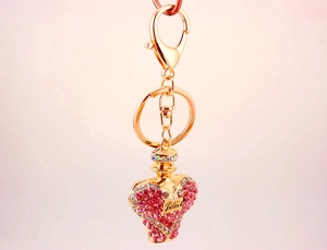 Close-up of golden perfume bottle keychain with pink crystals and Juliet engraving