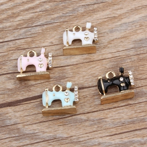 Sewing machine pendants in gold alloy with enamel and rhinestones on wood backdrop
