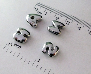 Vista macro di ciondoli a lettere d'argento 8mm con strass accanto a un righello