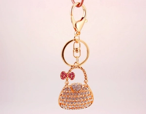 Close-up of golden metal handbag keychain with pink rhinestones and a bow charm detail