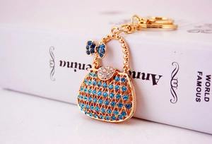Detailed view of golden handbag keychain with sparkling blue rhinestones and bow accent