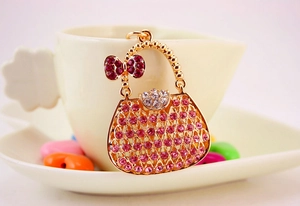 Dettaglio di un portachiavi a mini borsa dorata con strass rosa e un fiocco rosso decorativo