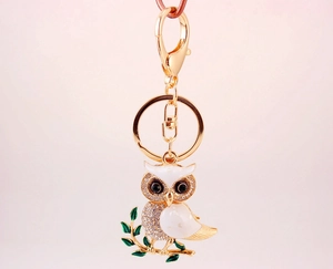 Close-up of golden owl keychain featuring white enamel and sparkling crystal accents