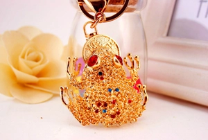 Nahaufnahme des goldenen Frosch-Schlüsselanhängers mit roten Steinen und Glücksgravur