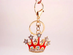 Detailed macro view of a gold-plated crown keychain with red crystals and rhinestones
