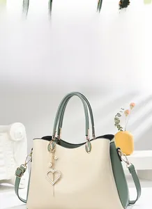 Nahaufnahme einer zweifarbigen Handtasche in Creme und Grün mit Goldlogo und Herzanhänger