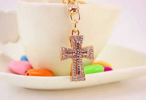 Detailed close-up of golden cross keychain with rhinestones hanging on a white ceramic cup