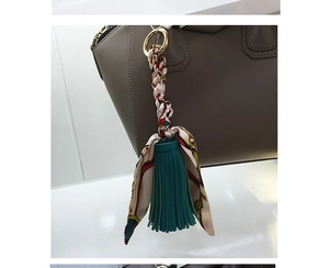 Dettaglio del ciondolo in pelle verde scuro con foulard in seta su una borsa