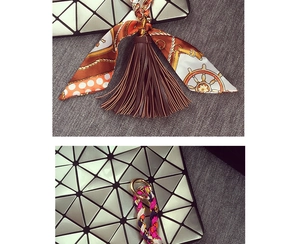 Dettaglio del portachiavi con nappa in pelle marrone e foulard su una borsa geometrica