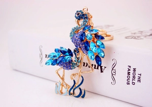 Détail du porte-clés flamant rose avec cristaux bleus et fermoir mousqueton sur un livre