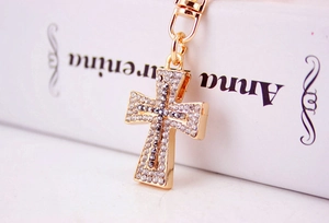 Detailed view of golden cross keychain with shimmering rhinestones on white book background