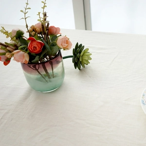 Close-up of beige cotton linen tablecloth with a decorative glass vase in soft sunlight