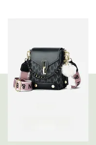 Close-up of black leather crossbody bag with gold lock, logo strap and plush charm