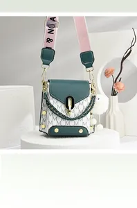 Close-up of green and white crossbody bag with wide strap and plush pendant on stand